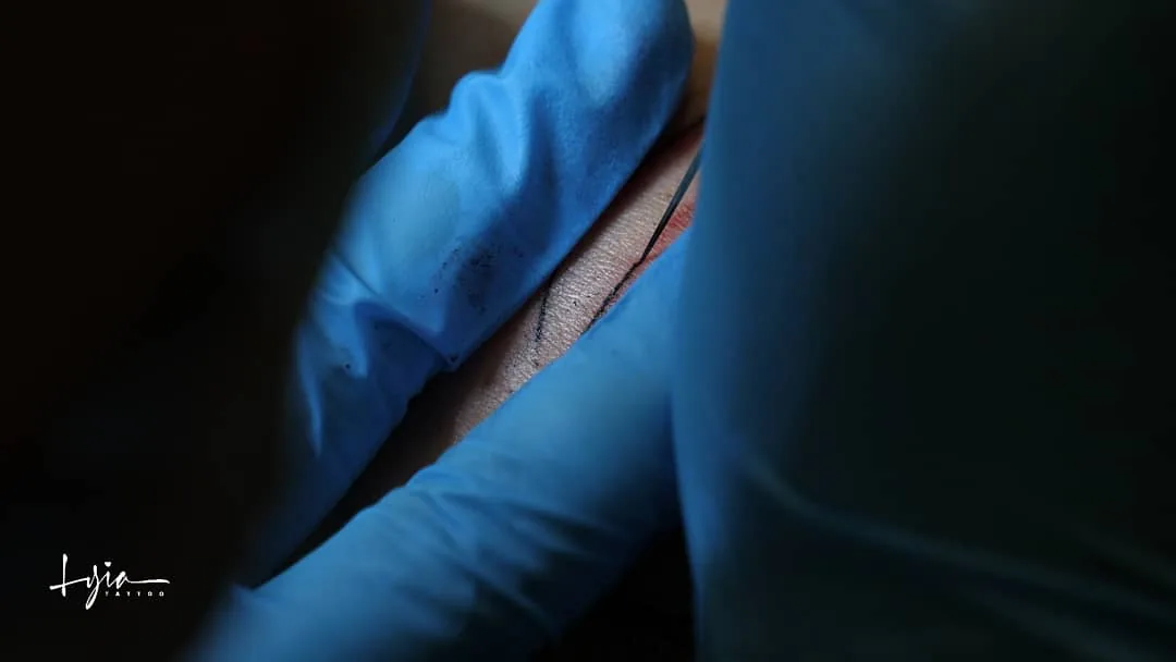 Tatouage handpoke en cours — gants bleus et aiguille